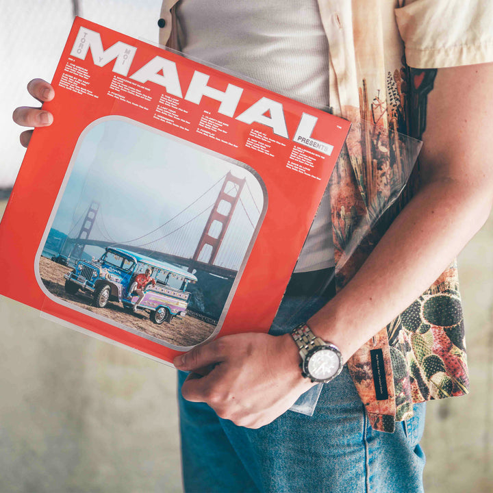 A person wearing a watch holds a red vinyl record cover titled “MAHAL”—featuring the Golden Gate Bridge and a colorful jeepney—safeguarded by Groove Guardian Premium 12" LP Outer Record Sleeves.