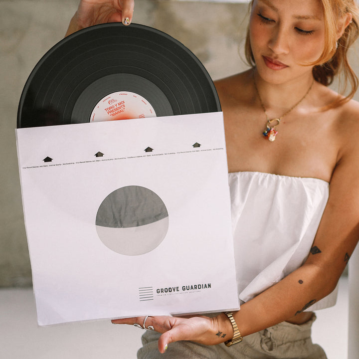 A woman in a white top holds a black vinyl partially out of a pristine Groove Guardian Ultra-Premium 12" LP Inner Record Sleeve. As she looks down at the record, her arm tattoos visible, the stylish sleeve keeps her vinyl collection protected and looking sharp.